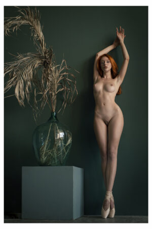 Fotografía de una mujer desnuda en punta con zapatillas de ballet en un fondo color esmeralda y un jarrón grande al lado.